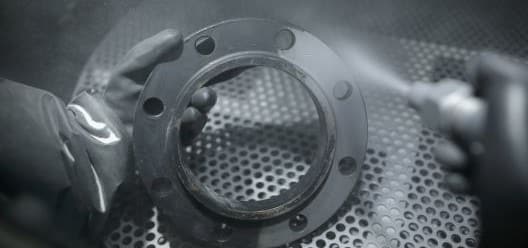 A metal part being finished in a hand air blast cabinet